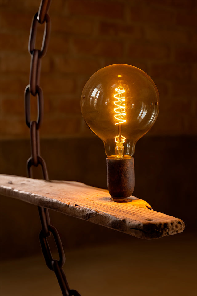 Primo piano della lampadina LED accesa su tavoletta in legno vissuto, con catena metallica e atmosfera calda in ambientazione indoor