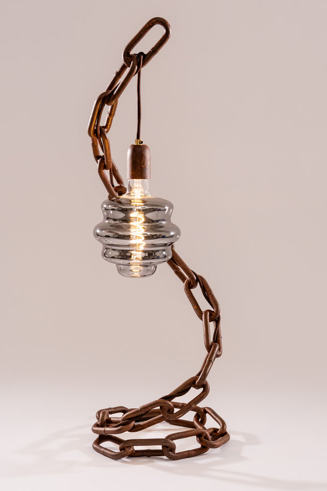 Lampada Onda con catena arrugginita modellata a spirale e lampadina decorativa in vetro fumé, sospesa con cavo elettrico visibile alla base