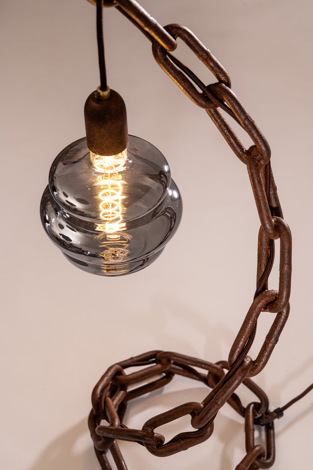 Vista dall’alto della lampada Onda con catena navale scultorea, vetro fumé e luce accesa. Il cavo nero è intrecciato tra le maglie