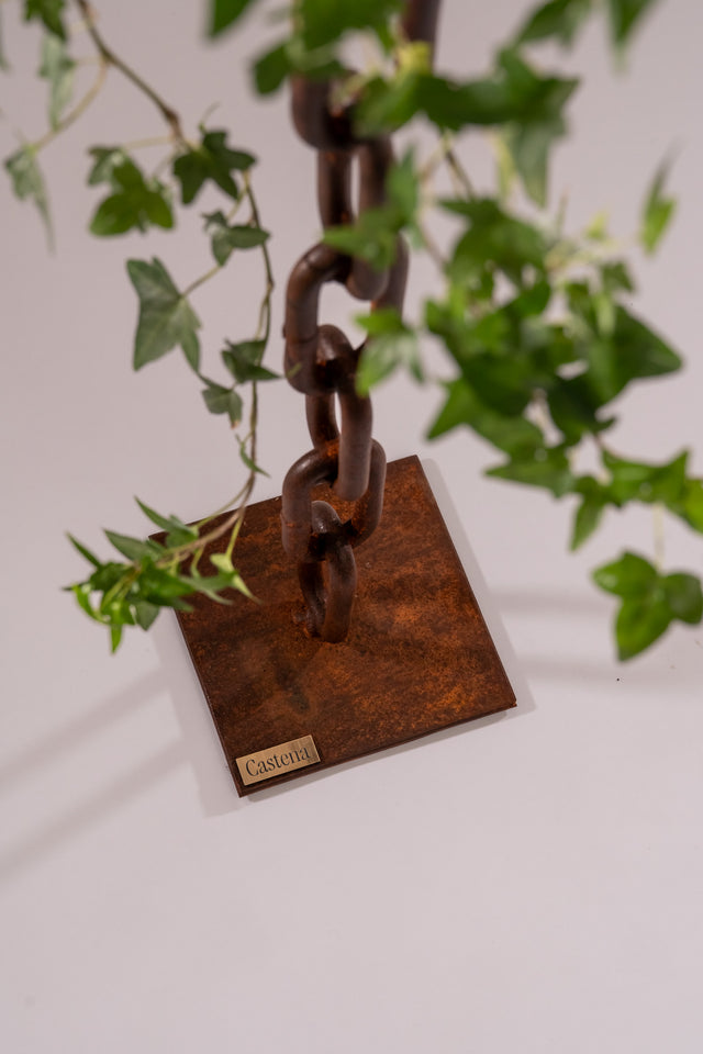 Dettaglio ravvicinato della base del porta candele Castena con catena marina arrugginita e foglie verdi decorative in primo piano